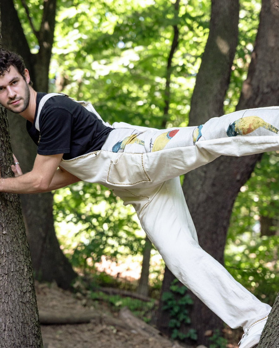 White overalls with hand-painted fruit detail, leaning against a tree