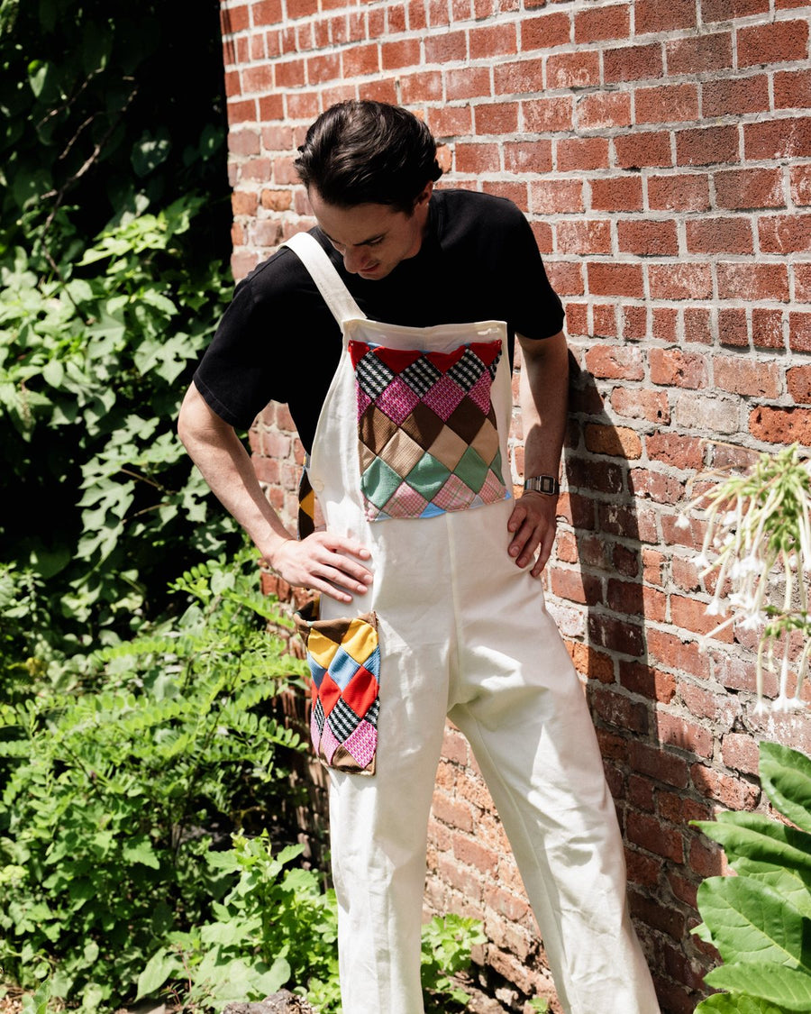 White overalls with a multicolour patchwork bib, against a brick wall